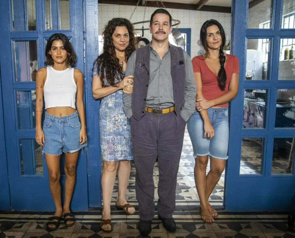 Maria (Isabel Teixeira) entra em casa pelos fundos para passar batido enquanto Tenório (Murilo Benício) e Guta (Julia Dalavia) almoçavam sozinhos à mesa, servidos por Zefa (Paula Barbosa)